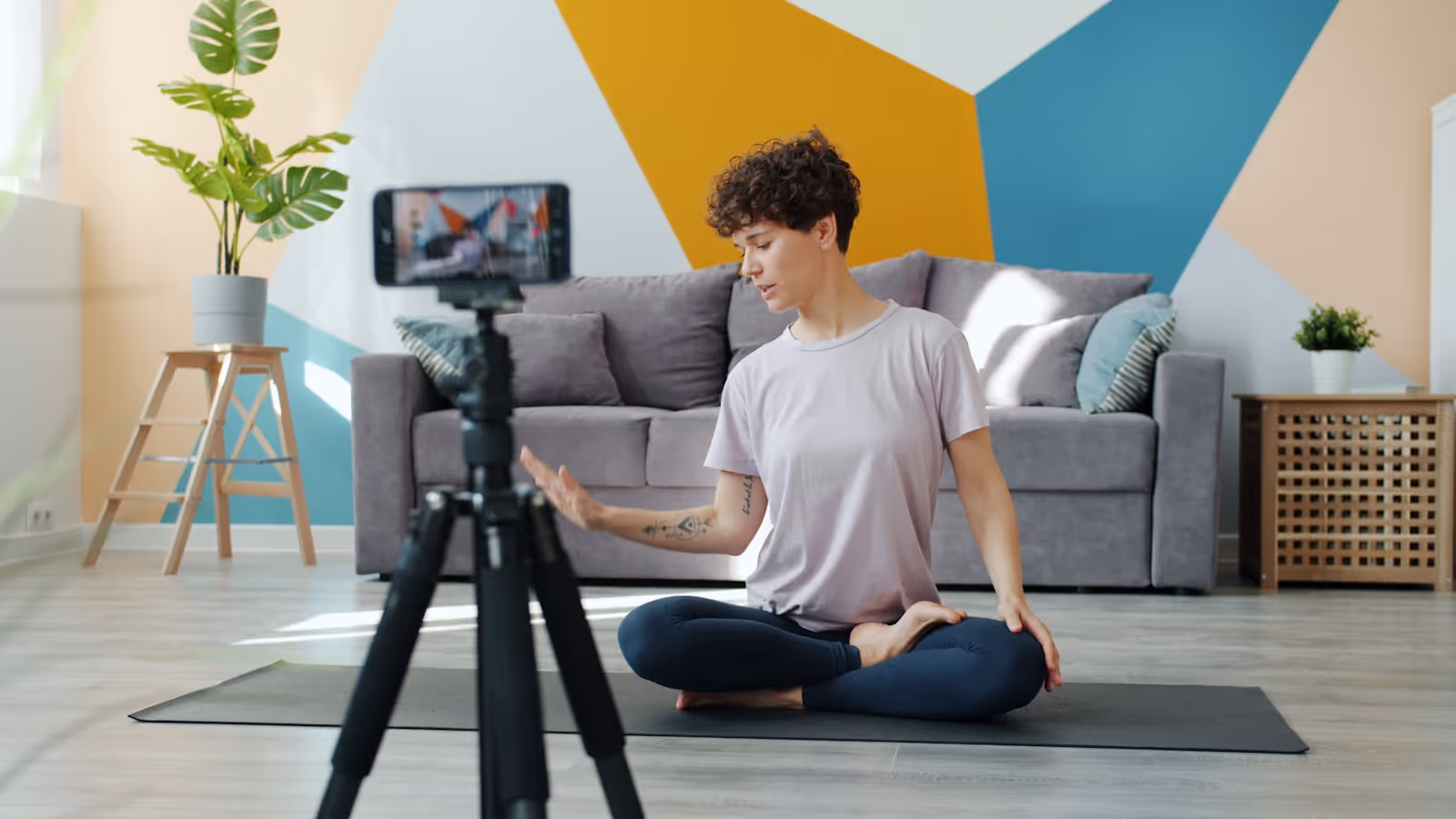 Une prof de yoga assise en tailleur consulte son téléphone pour préparer une publication